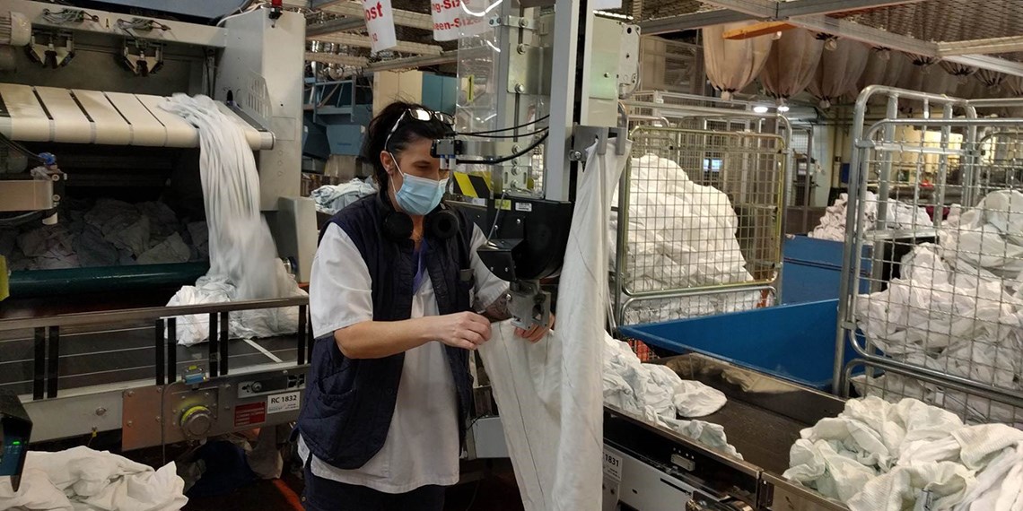 En person i tvättindustrin, med munskydd på, i fullt arbete på sin arbetsplats.
