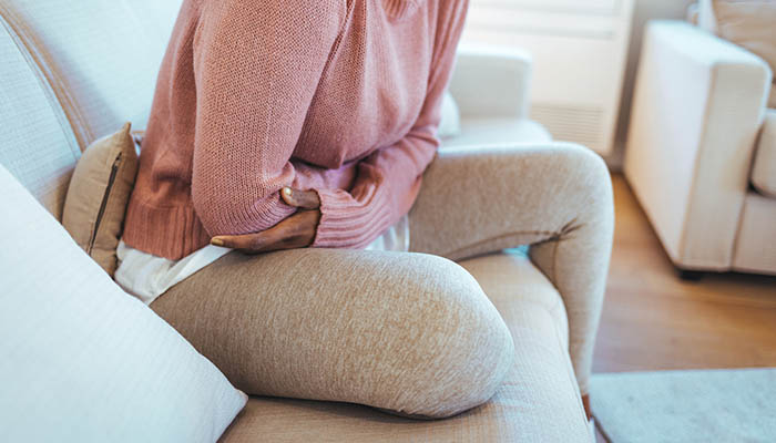 Kvinna som sitter ner och håller om sin mage