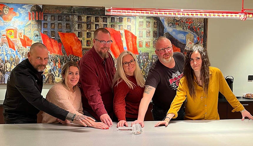 Personer som står vid ett bord. Alla har sin ena hand på bordet. 