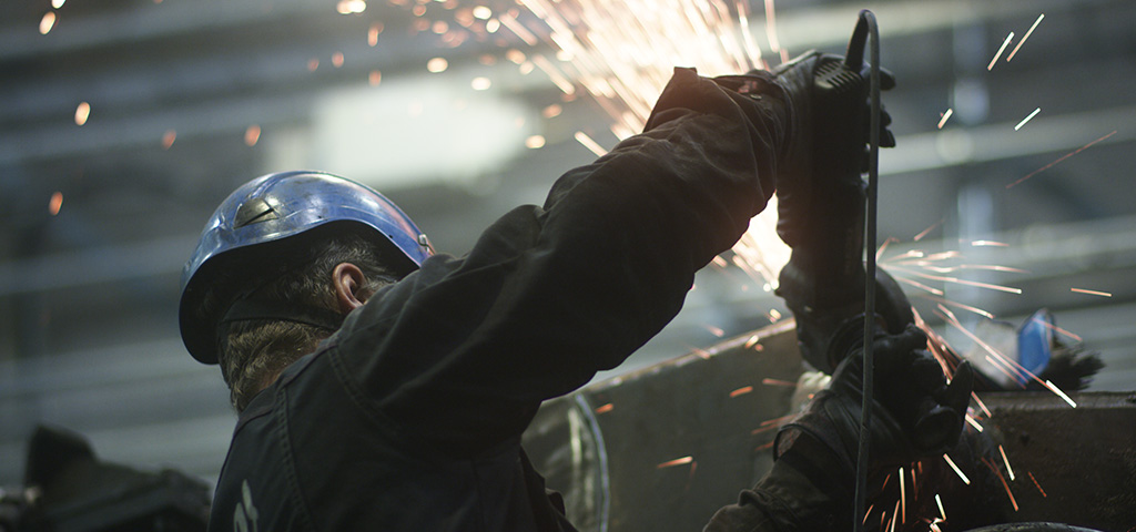 Person i arbetskläder och hjälm svetsar.