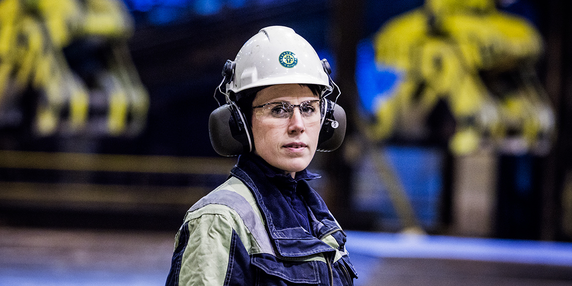 Person i arbetskläder och hjälm med skyddsombudsmärke.