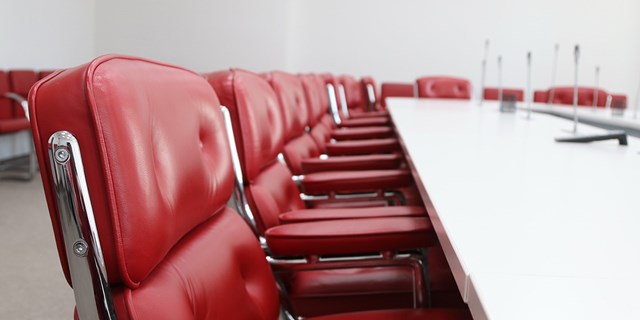 Bild av ett vitt mötesbord med röda stolar.