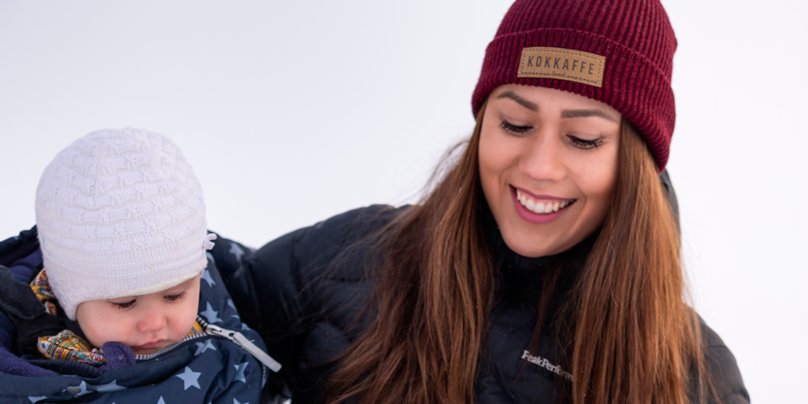 Porträttbild av Lina Nyberg, ordförande för ungdomskommittén i IF Metall Malmfälten, vinterklädd med yngsta barnet i famnen.