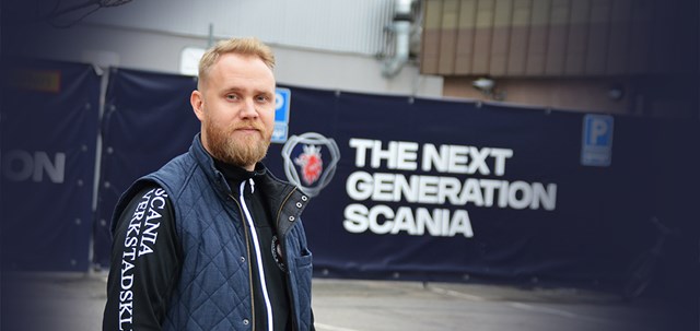 Erik Eklund på arbetsplatsen framför skylt med texten "The next generation Scania".