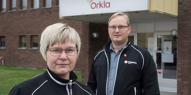 Två personer i svarta jackor framför företaget Orkla.