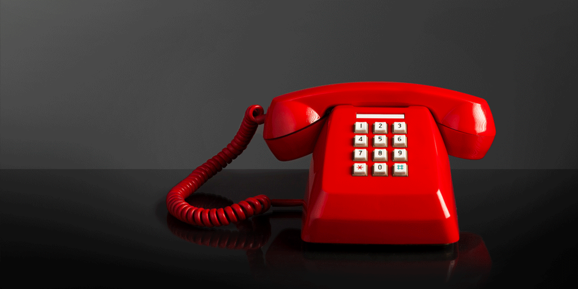 Röd retrotelefon mot mörk bakgrund.