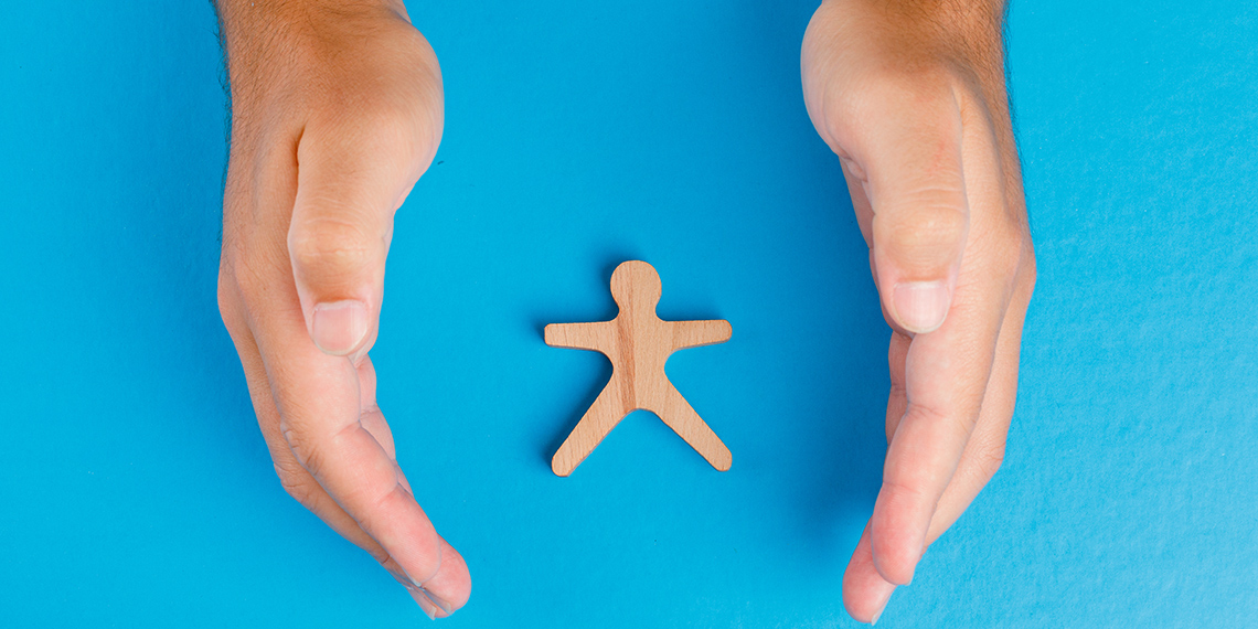 Händer som kupas runt en träfigur, ljusblå bakgrund.