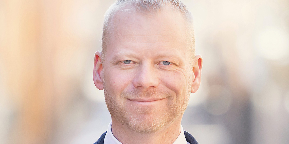 Porträtt av person utomhus mot suddig bakgrund.