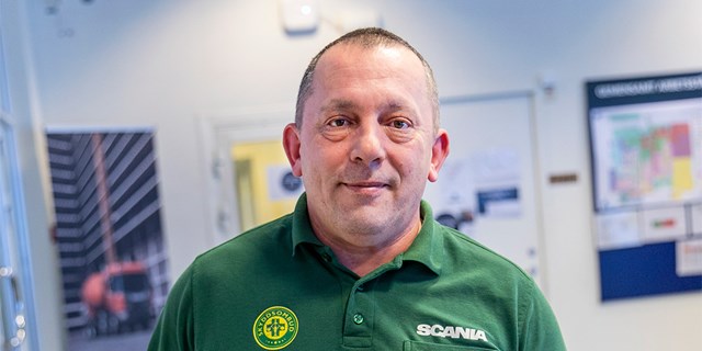 Person i grön tröja med skyddsombudsmärke och logotyp från Scania.