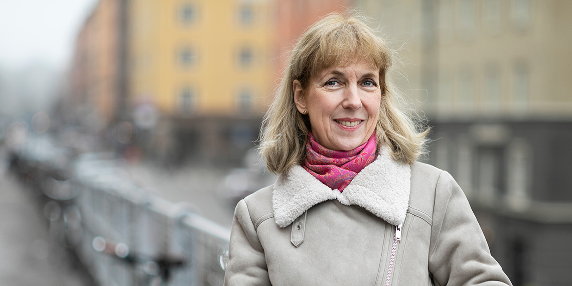 Person i ljus jacka och cerice halsduk i stadsmiljö utomhus.