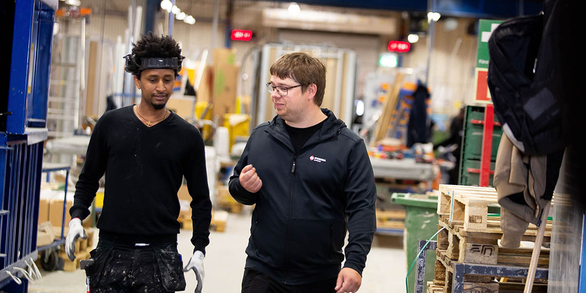 Två män som går i industrimiljö och pratar med varandra 