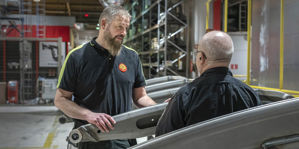Robert Wallgren står och pratar med en person som har ryggen mot kameran. Det står i industrimiljö.