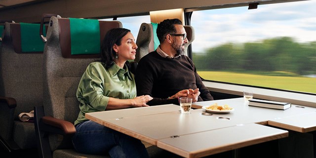 Bilden visar två personer som leendes åker tåg med SJ och tittar ut genom fönstret.