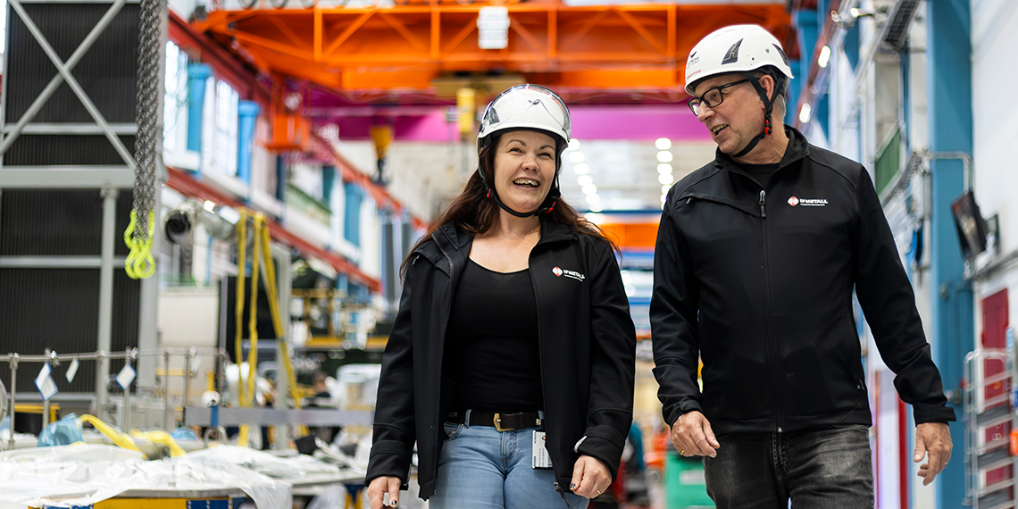 Jenny Holgersson och Kennet Andersson gående i fabriksmiljö. De båda ler.
