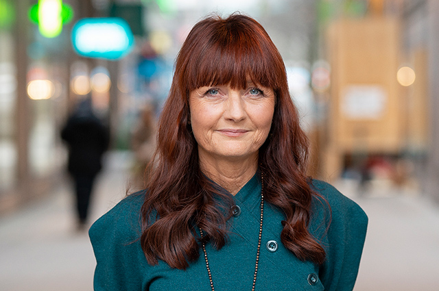 Marie Nilsson i blågrönt framför suddig stadsbakgrund.